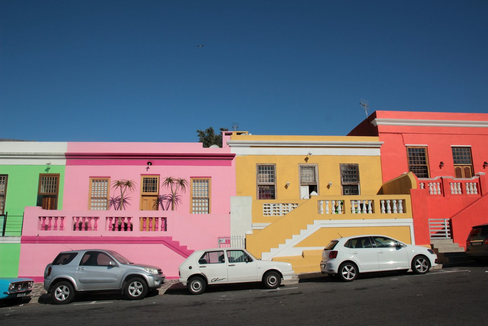 A terrace of vividly painted houses in the Bo-Kaap with cars parked along the street.