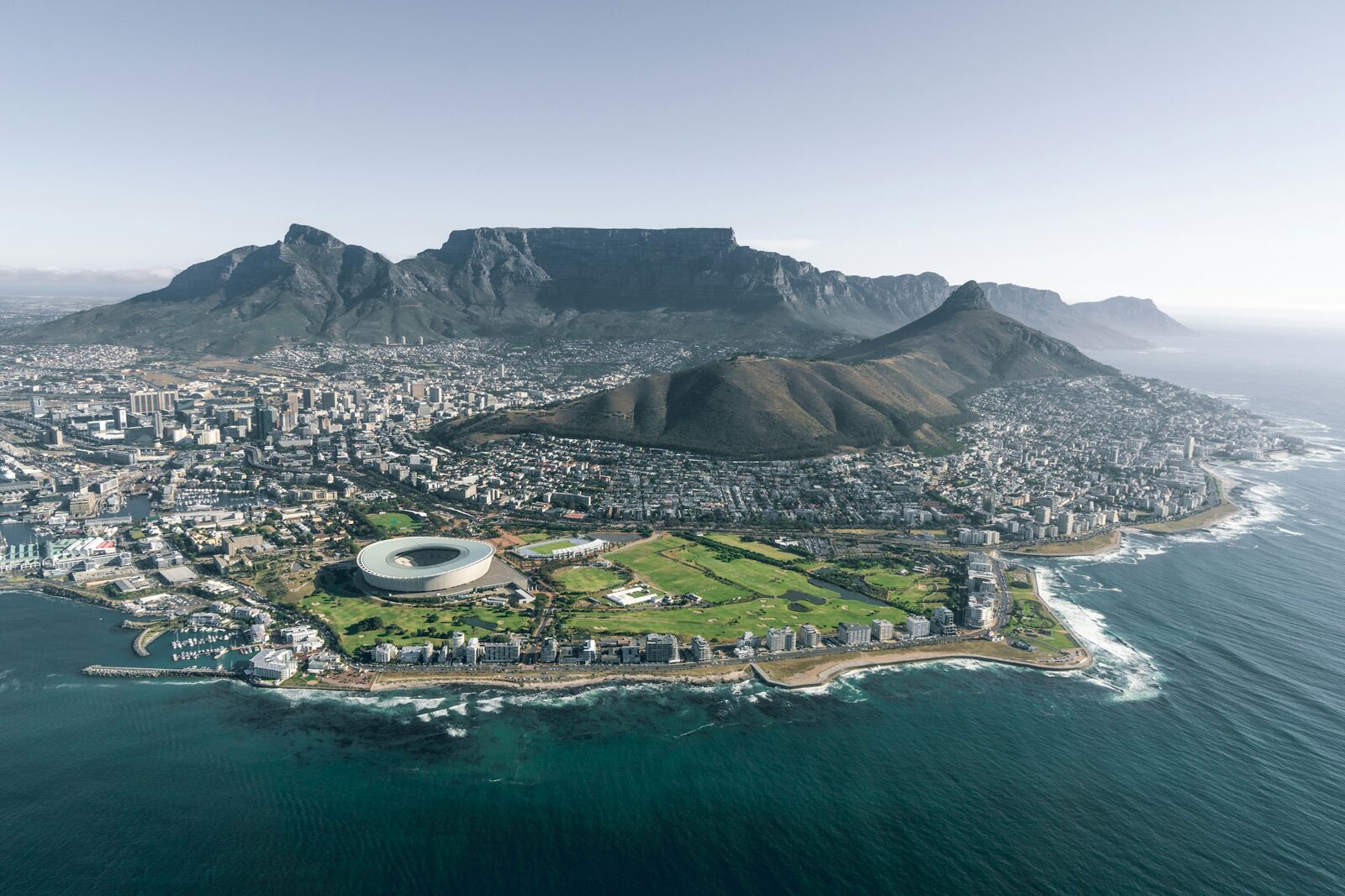 An aerial view of Cape Town with Table Mountain rising behind the city and the Atlantic Ocean beyond.